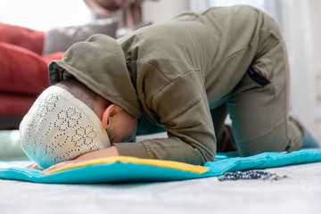 Little boy wearing green clothes and wearing a fez is praying.