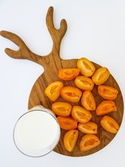 Apricot slices on a wooden cutting Board and a glass of milk on a white background.