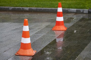 Side view of two bright orange-white warning cones on brick pavement, traffic is blocked, warning signal