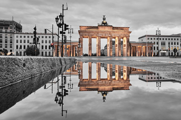 Brandenburg gate after the rain, beautiful reflection of the yellow golden gate in the water of a street puddle, grey sky with clouds in the background © Peter Jesche