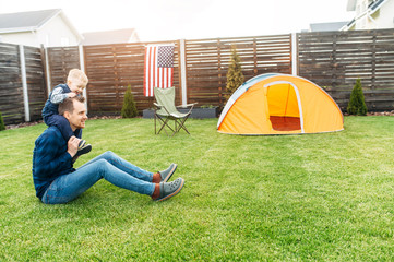 Young father and his cute toddler boy camped in the backyard, they are playing funny on a lawn....