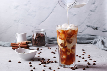 Cold coffee in a tall glass with cream being poured into it showing the texture of the drink. Light...