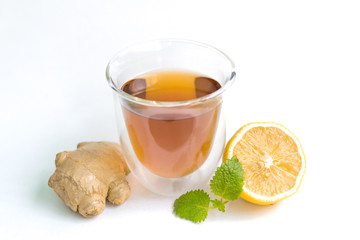 transparent glass with tea and fresh ginger root with lemon and mint or melissa leaves on a white isolated background
