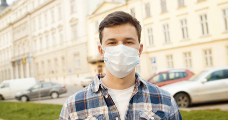 Young man standing outdoors in protective medical mask on face.
