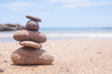 Fototapeta na wymiar Five stones balanced on the sand close to the ocean at the beach.