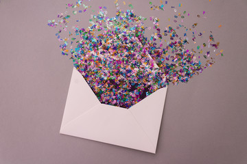 Opened white envelope with multicolored sparkle glitter confetti letters on pastel lilac background. Festive greeting concept. Flat lay style. Top view