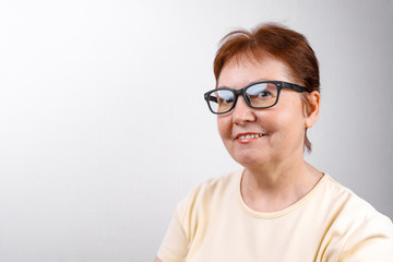 senior woman looks away with glasses on a white background in a light T-shirt. place for text, isolated