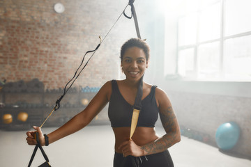 Stimulate your life now. Sportive woman smiling at camera, holding TRX fitness straps while having...