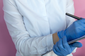 Female doctor in blue latex gloves makes notes on a hospital note.