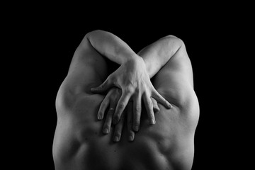 Male model athlete with muscular sexy body and bare back. Man's back and hands on a black background. Pumped back and arms.
