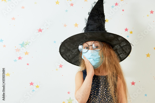 Happy Halloween on quarantine coronavirus pandemic. Little girl child in witch carnival costume and face protection mask.