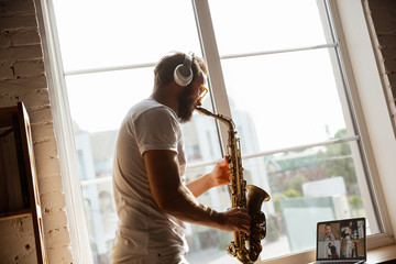Caucasian musician playing saxophone during online concert at home isolated and quarantined. Using...
