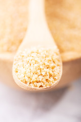 Uncooked bulgur in wooden spoon, rustic style. Bulgur wheat grains, healthy food
