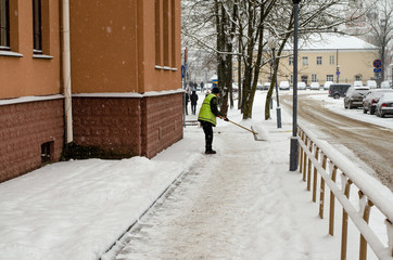 snow storm in the city. Roads and sidewalks covered with snow. Worker shovel clears snow. Bad...