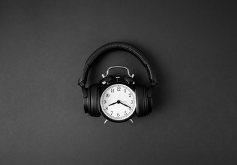 Black vintage alarm clock in headphones on abstract dark background with copyspace