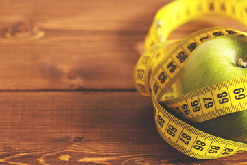 Tape measure and green apple on a wood background top view. The concept of a healthy diet, body weight control, down weight. Healthy lifestyle. Copy space