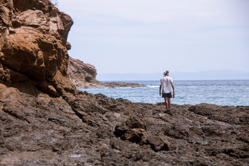 A man standing at the rocks looking at the horizon at the sea s