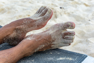 Brown man feet sprayed with summer beach sand