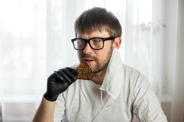 COVID-19. Young caucasian man in glasses, white mask and black gloves with a slice of bread in his...