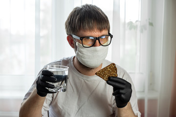 COVID-19. Young caucasian man in glasses, white mask and black gloves with a slice of bread in his...