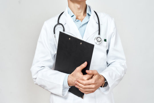 Doctor at work. Cropped photo of professional doctor in medical uniform with stethoscope around neck holding black paper folder, standing against grey background