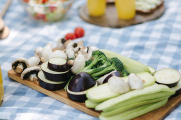 Slised vegetables on wooden board outside. Fresh vegetables outdoors on checkered napkin. Zucchini, eggplant, mushrooms and broccoli