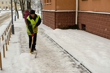 snow storm in the city. Roads and sidewalks covered with snow. Worker shovel clears snow. Bad...