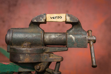 Vice grip tool squeezing a plank with the word verso