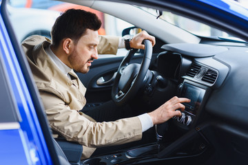 Handsome bearded buyer in casual wear in dealership, guy looks on camera while standing near car...