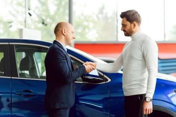 Car salesman handing over the keys for a new car to a young businessman