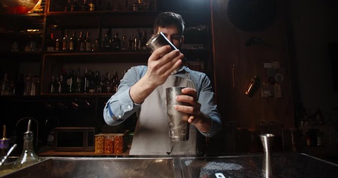 Cool professional caucasian bartender making a cocktail, muddling ice with beverage in his shaker. Authentic barman making alcohol drink using special equipment 4k footage
