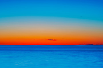 Fototapeta na wymiar Vibrant colored summer sunset reflecting in ocean with endless horizon and deep blue ocean at island of Gotland in Sweden