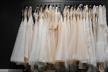 Wedding dresses made of silk chiffon, tulle and lace. Beautiful White cream bridal dress on hangers in wedding salon. Pearls and crystals pendants on the sleeves of a delicate color of a wedding dress