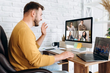 Work online by a video conference with colleagues. A man in a stylish wear sits at his workplace at home and solves working issues on video communication with business partners