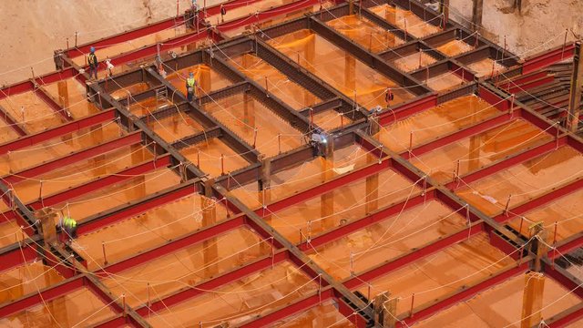 Steel frame of basement, modern tower construction site, welding works. Time lapse shot, one man do welding, several engineers control around area. Safety nets hang at open spaces