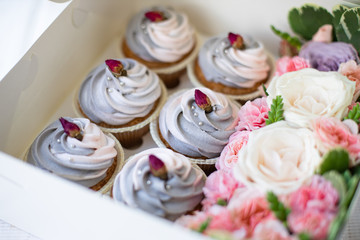 closeup of delicious sweet muffins with pink-gray butter cream in a box with flowers