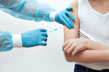 a doctor in blue medical gloves makes an injection to the patient, preventive vaccination in the shoulder, a disposable syringe in the doctor’s hands, the concept of immunity