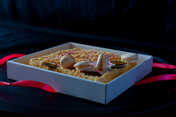cake with macaroons with colored crumbs on a round black dish, on a dark background. Copy space. on a dark background