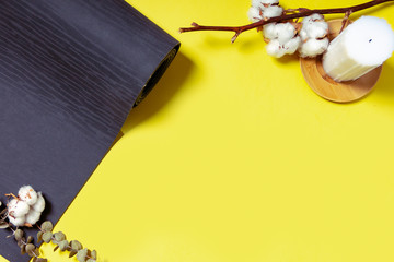 Natural wooden colored wax candle with cotton branch and rolled black yoga, pilates mat on the yellow background. Top view and space for text. Relax and meditation concept