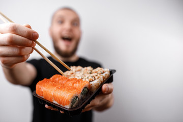 young man in a black T-shirt eats sushi rolls