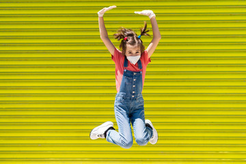 Child girl jumping wearing a protection mask against coronavirus