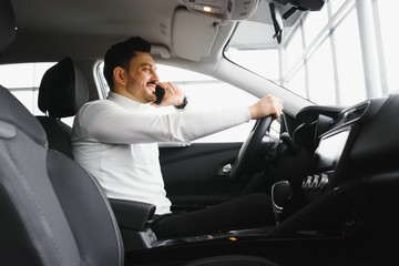 Nice business talk. Handsome young businessman talking on his smart phone and smiling while sitting on the front seat