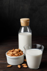 Almond milk in a glass and a glass bottle on dark wooden background