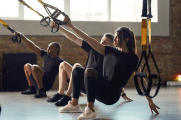 Power Performance. Full-length shot of men and women doing fitness TRX training exercises at industrial gym. Push-up, group workout concept