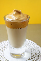 One glass with a Dalgona coffee cocktail, front view. Trendy Korean quarantine drink on a yellow. 