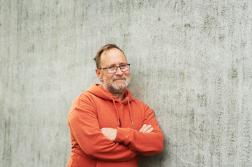 Outdoor portrait of handsome middle age man posing against grey urban wall, wearing bright orange...