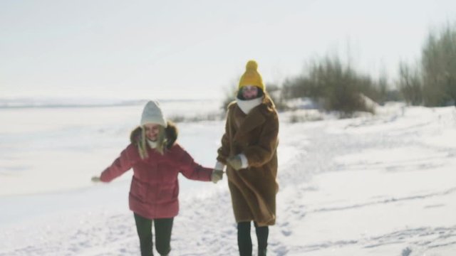 Two women friends holds each other's hands and runs on the snow