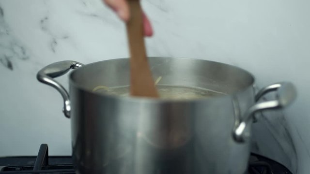 Close-up of mixing pasta/spaghetti in boiling water on a saucepan and pancetta in a frying pan