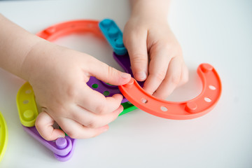 Close up of kid hands playing bright plastic toy constructor. Creative baby make new forms. copy...