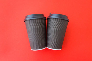 Coffee to go concept. Disposable black cup with spiral texture with black plastic cover on a trendy vivid red background. Place for text. Flat lay style. Top view.